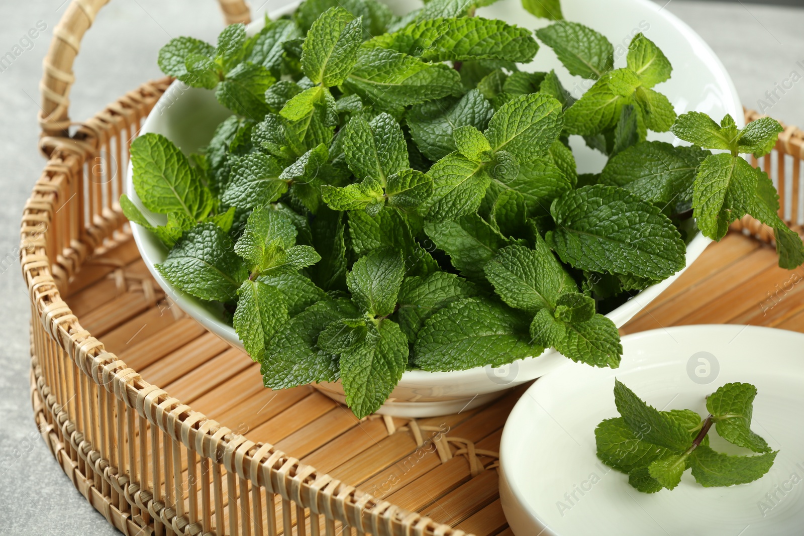Photo of Bowl of fresh green mint leaves on wicker tray, closeup