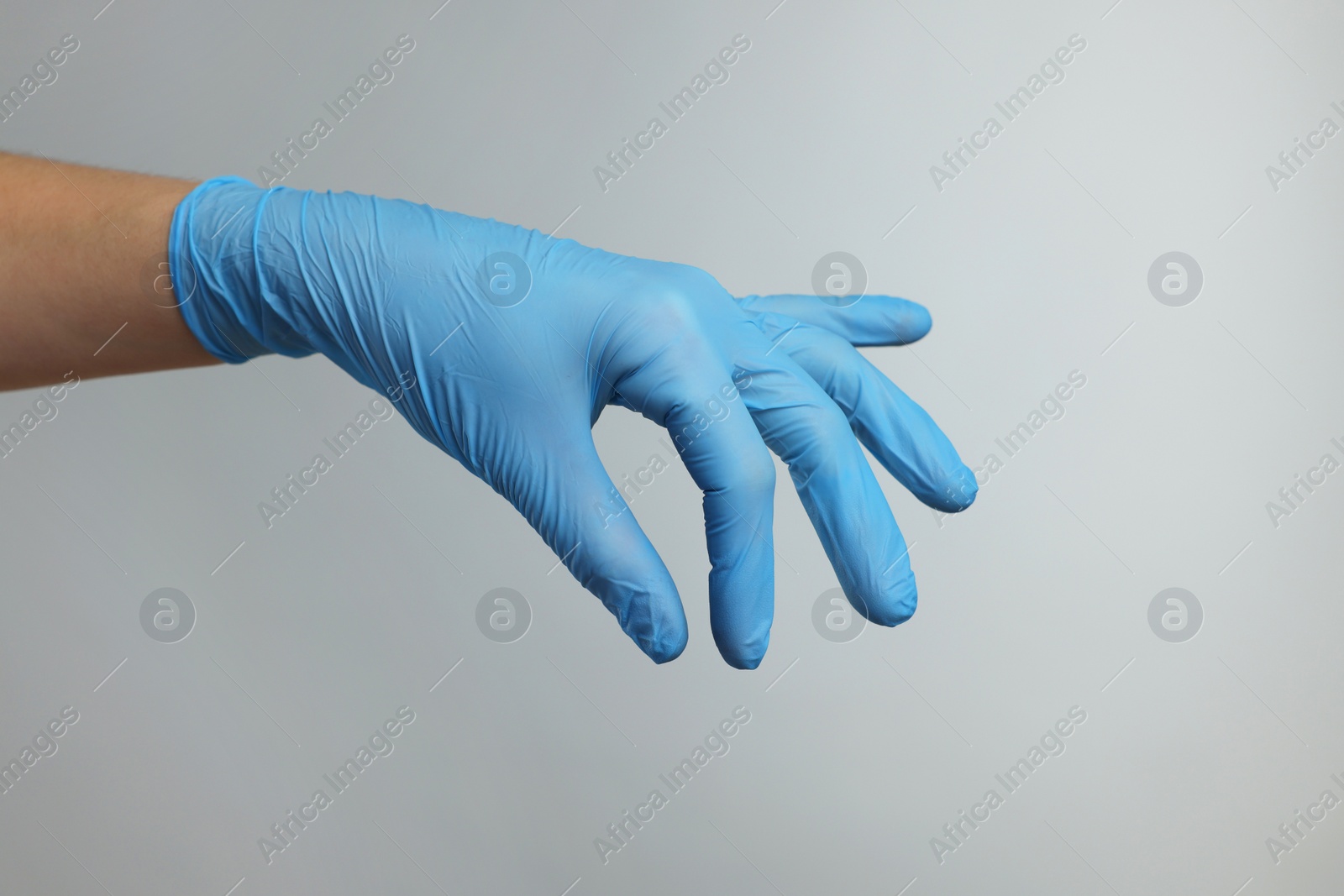 Photo of Doctor wearing light blue medical glove holding something on grey background, closeup