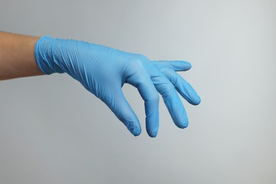 Doctor wearing light blue medical glove holding something on grey background, closeup