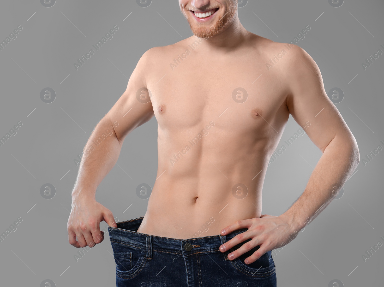 Photo of Young man with slim body in old big size jeans on grey background, closeup