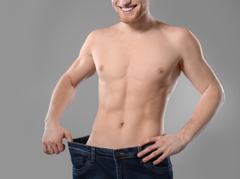 Photo of Young man with slim body in old big size jeans on grey background, closeup