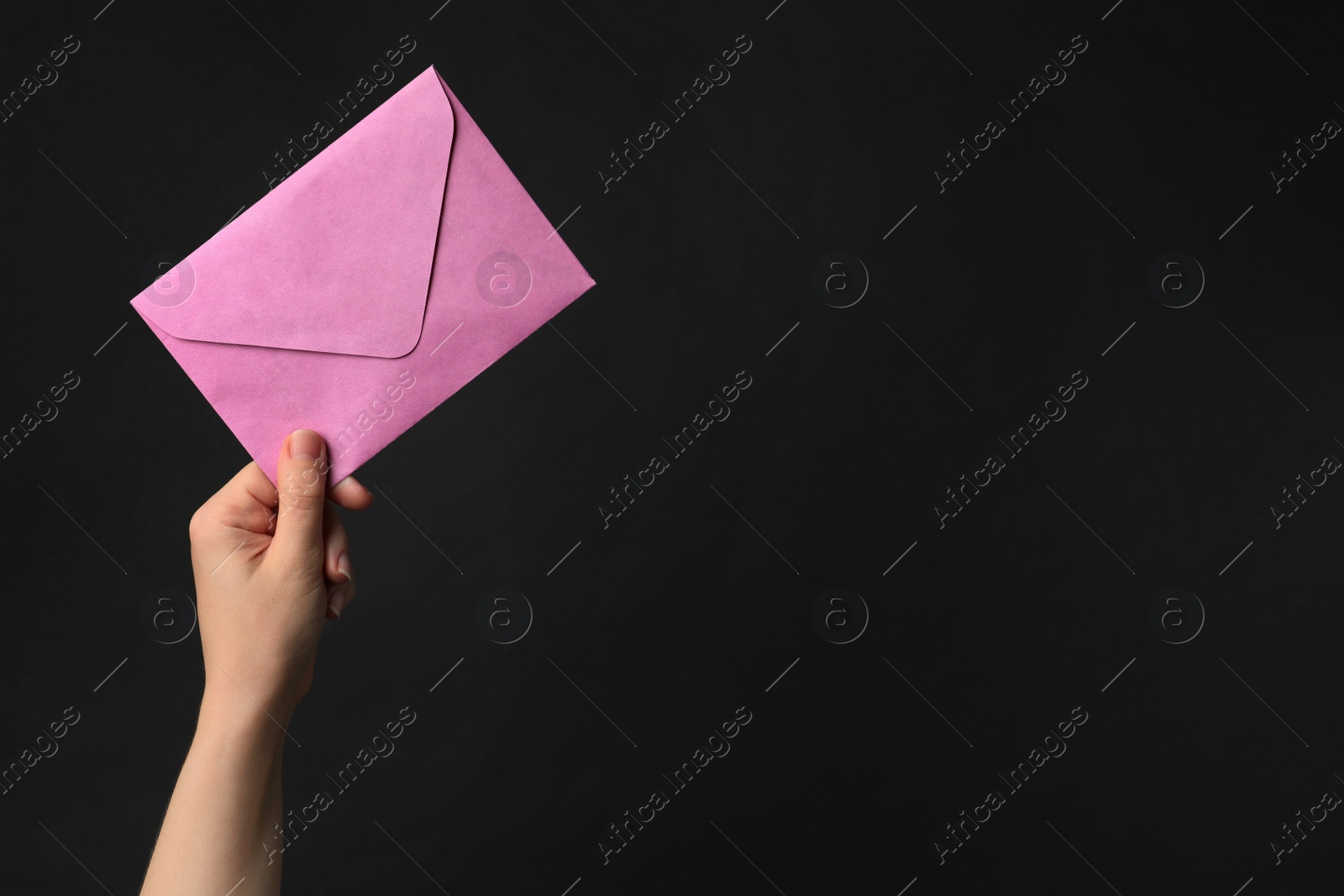Photo of Woman holding pink paper envelope on black background, closeup. Space for text
