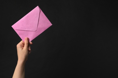 Woman holding pink paper envelope on black background, closeup. Space for text