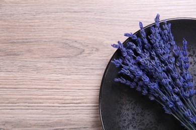 Bouquet of beautiful preserved lavender flowers and plate on wooden table, top view. Space for text