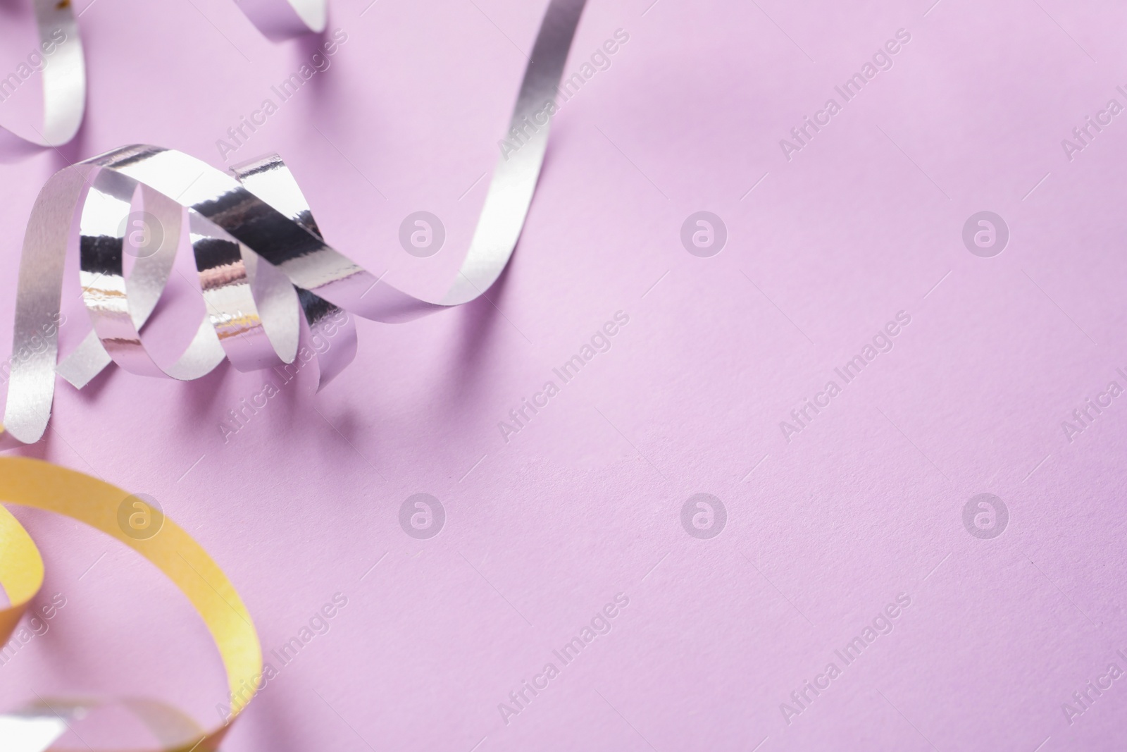 Photo of Shiny serpentine streamers on lilac background, closeup. Space for text