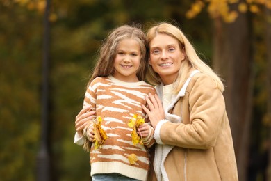 Portrait of happy mother and her daughter with dry leaves in autumn park