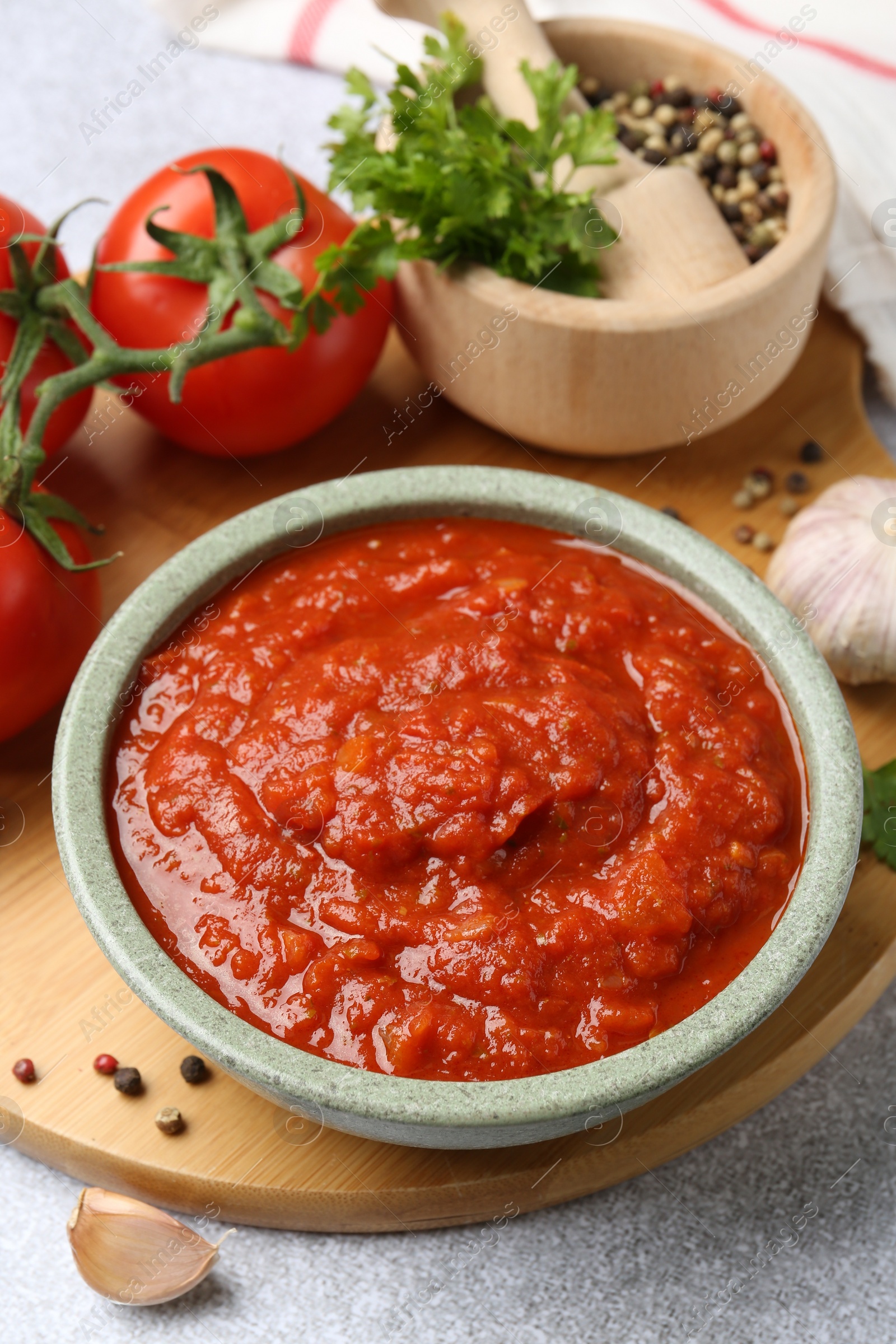 Photo of Homemade tomato sauce in bowl and fresh ingredients on light grey table