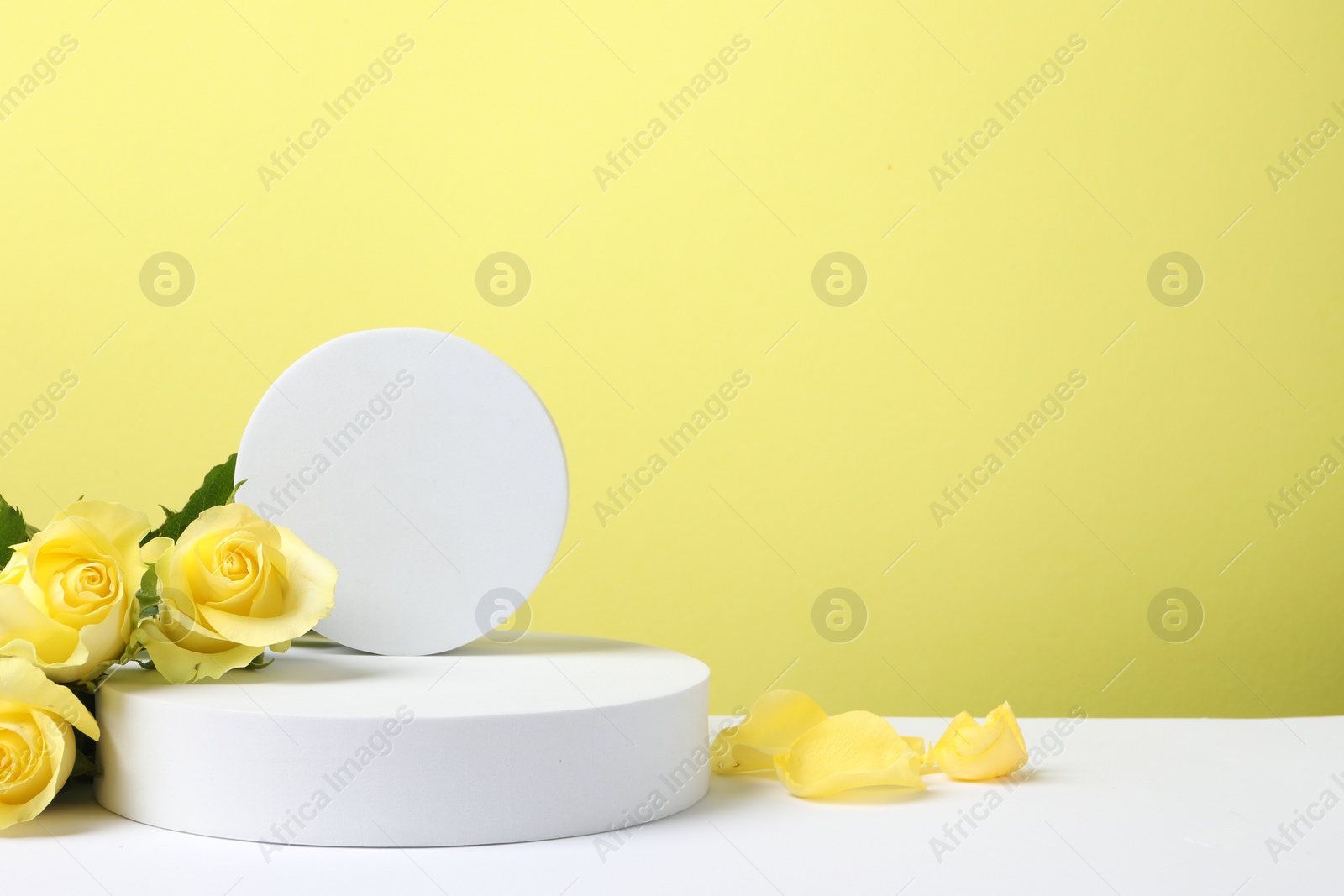 Photo of Beautiful presentation for product. Geometric figures and roses on white table against yellow background, space for text