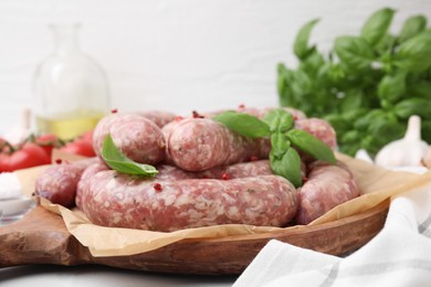 Raw homemade sausages, basil leaves and peppercorns on table, closeup
