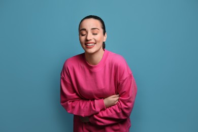 Photo of Beautiful young woman laughing on light blue background. Funny joke