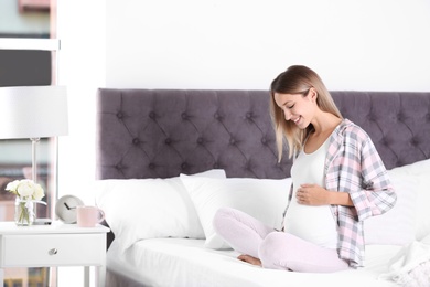 Happy pregnant woman sitting in bed at home