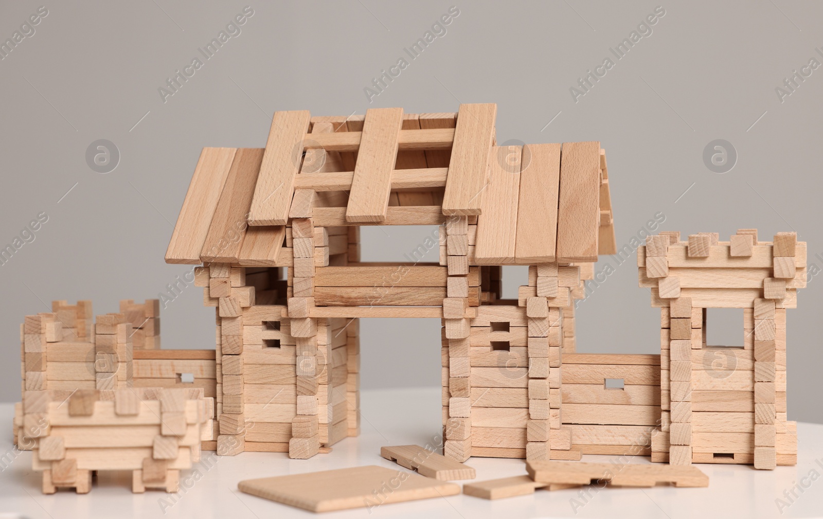 Photo of Wooden entry gate and building blocks on white table against grey background. Children's toy