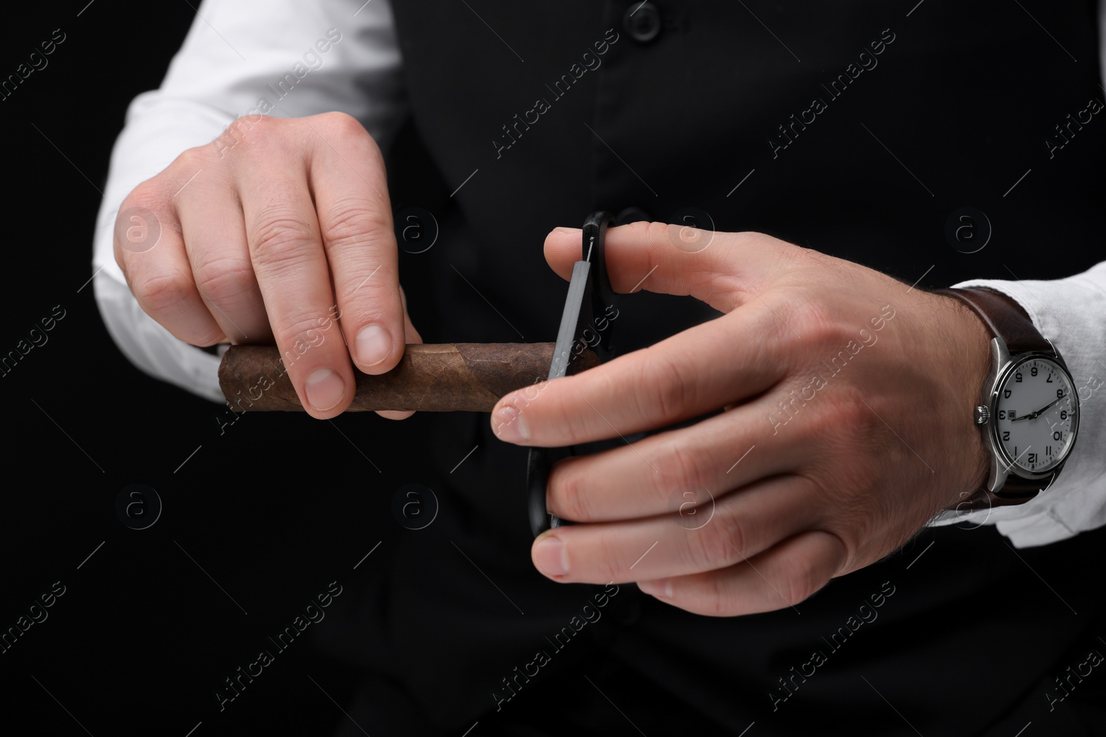 Photo of Man cutting tip of cigar on black background, closeup