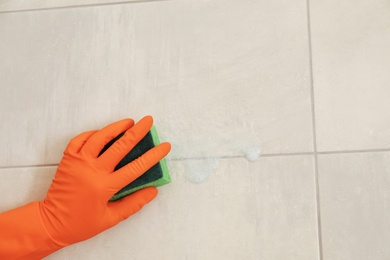 Photo of Woman in protective glove cleaning bathroom wall with sponge, closeup