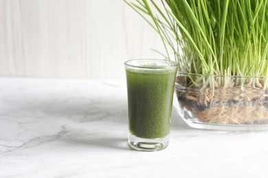 Photo of Wheat grass drink in shot glass and fresh sprouts on white marble table