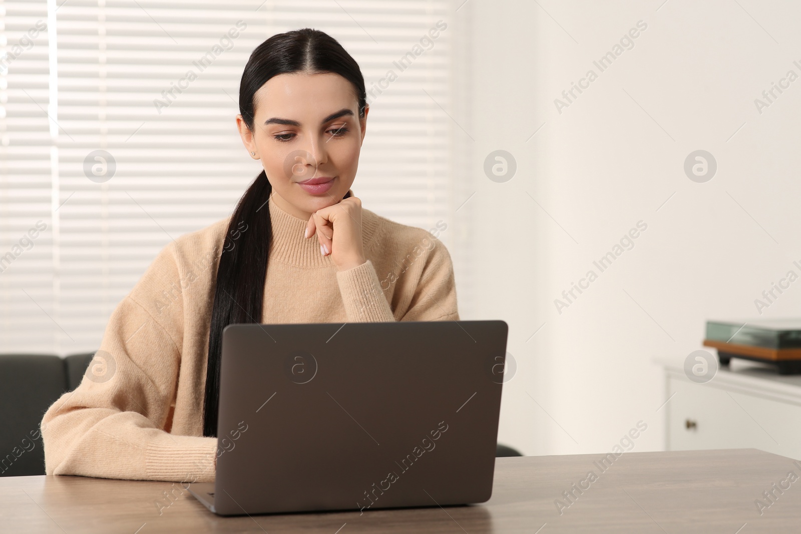 Photo of Woman working with laptop at wooden desk in room