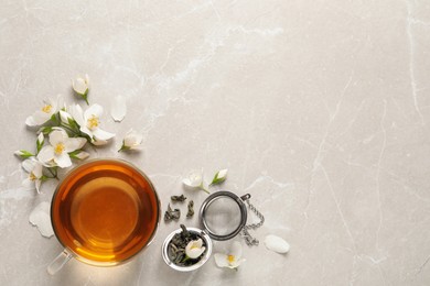 Glass cup of aromatic jasmine tea and fresh flowers on grey table, flat lay. Space for text