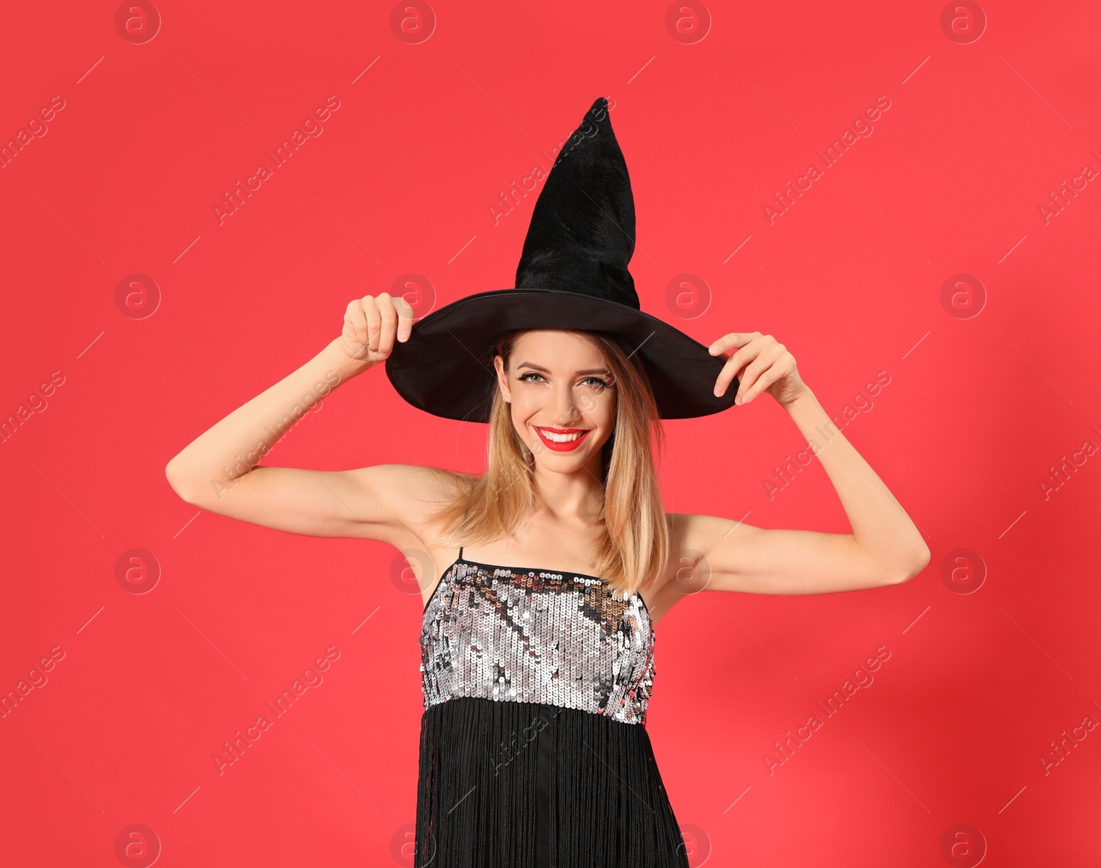 Photo of Beautiful young woman wearing witch costume for Halloween party on red background