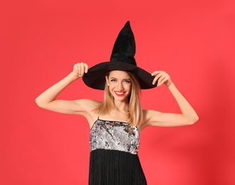 Photo of Beautiful young woman wearing witch costume for Halloween party on red background