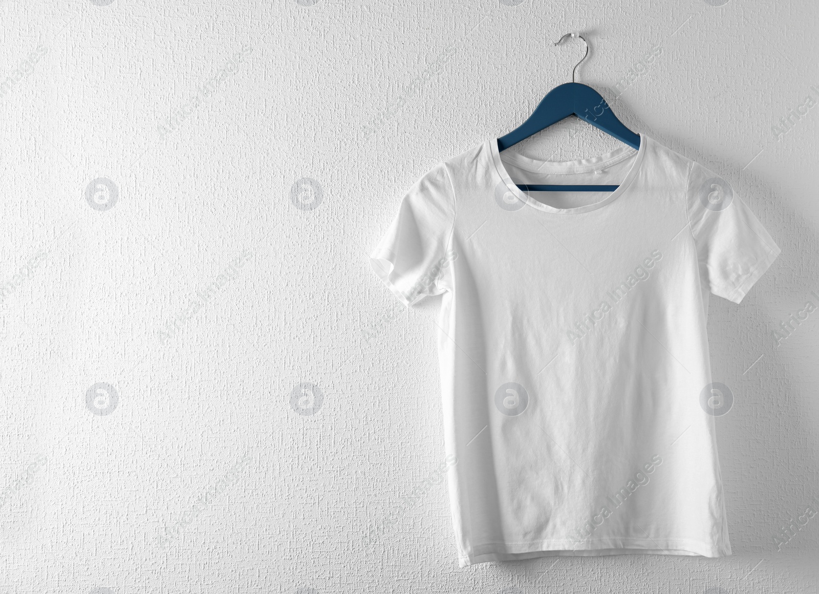 Photo of Hanger with white t-shirt on light background. Mockup for design