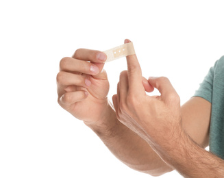 Photo of Man putting sticking plaster onto finger on white background, closeup