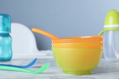 Plastic bowls and spoons on white marble table indoors. Serving baby food