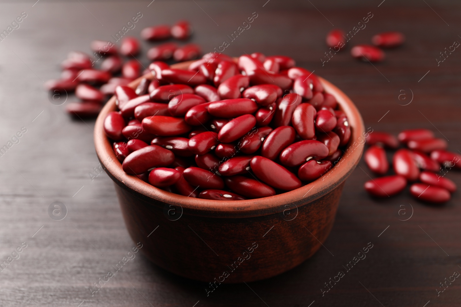 Photo of Raw red kidney beans in bowl on wooden table, closeup