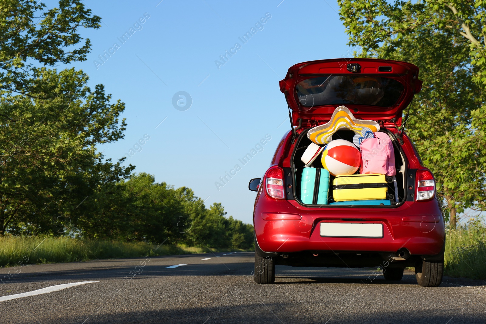 Photo of Family car with open trunk full of luggage on highway. Space for text