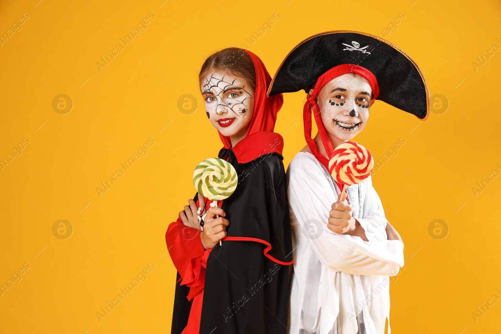 Photo of Cute little kids with lollipops wearing Halloween costumes on yellow background