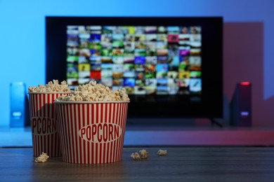 Photo of Modern TV set indoors, focus on buckets of popcorn