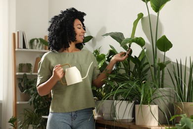 Happy woman watering beautiful potted houseplants at home