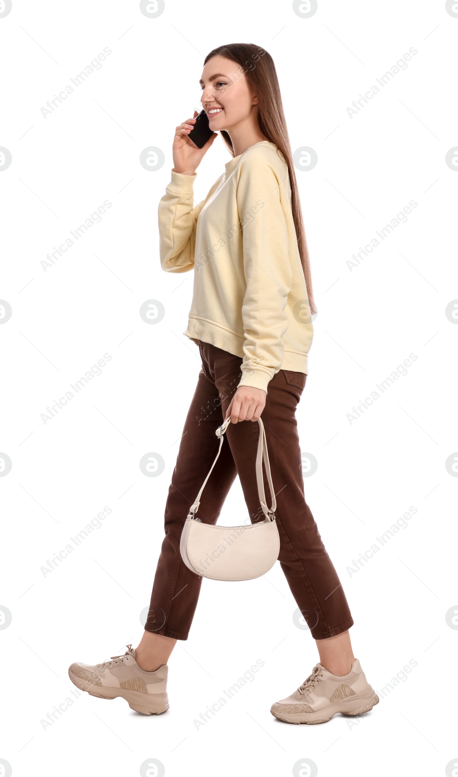 Photo of Young woman in casual outfit talking on smartphone while walking against white background