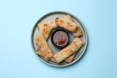 Photo of Fried spring rolls and sauce on light blue table, top view