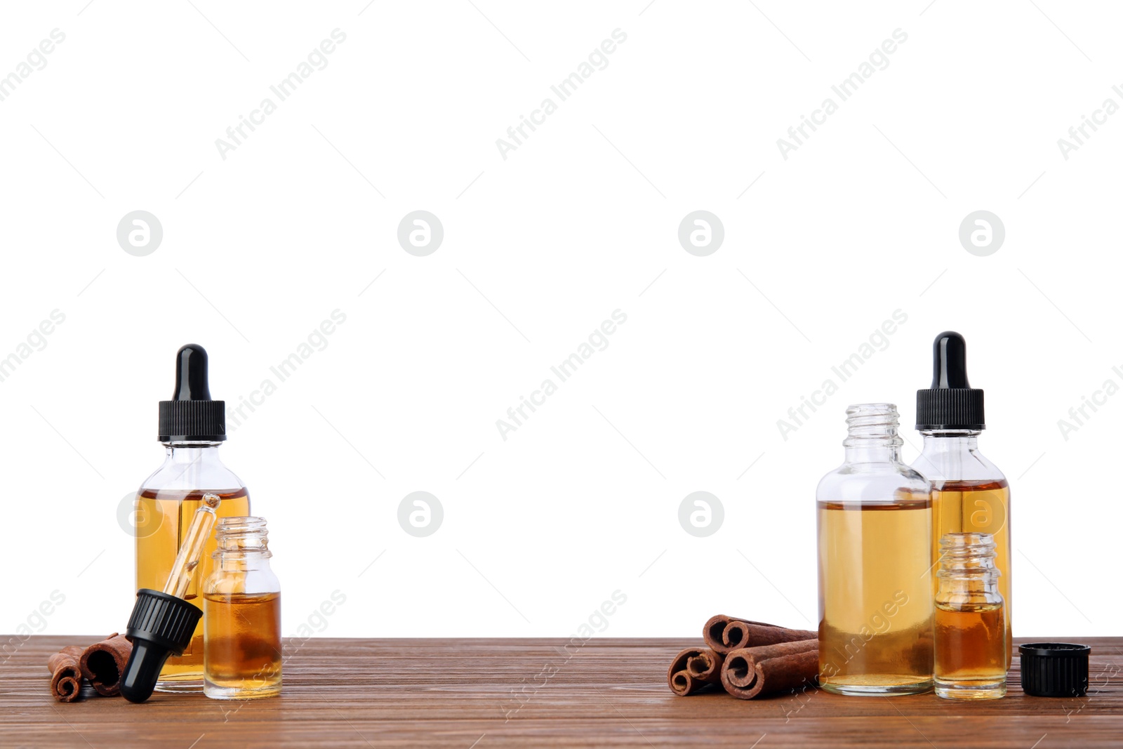 Photo of Bottles of essential oils and cinnamon sticks on wooden table against white background. Space for text