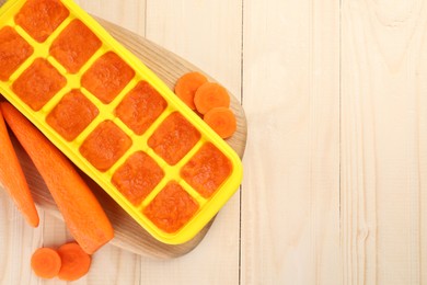 Photo of Carrot puree in ice cube tray and fresh carrot on wooden table, top view. Space for text