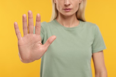 Photo of Woman showing stop gesture on yellow background, closeup