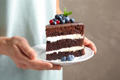 Photo of Woman holding plate with slice of chocolate sponge berry cake on grey background, closeup