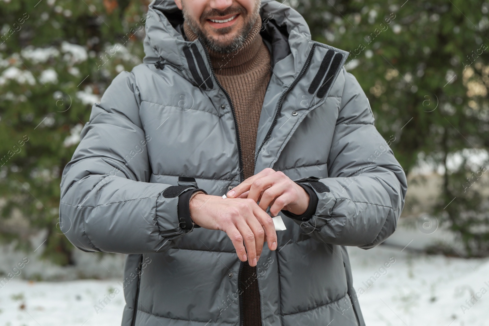 Photo of Man applying cream from tube onto hand outdoors, closeup. Winter care