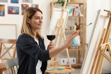 Photo of Beautiful woman with glass of wine painting in studio. Creative hobby