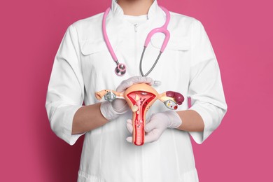 Photo of Doctor demonstrating model of female reproductive system on pink background, closeup. Gynecological care