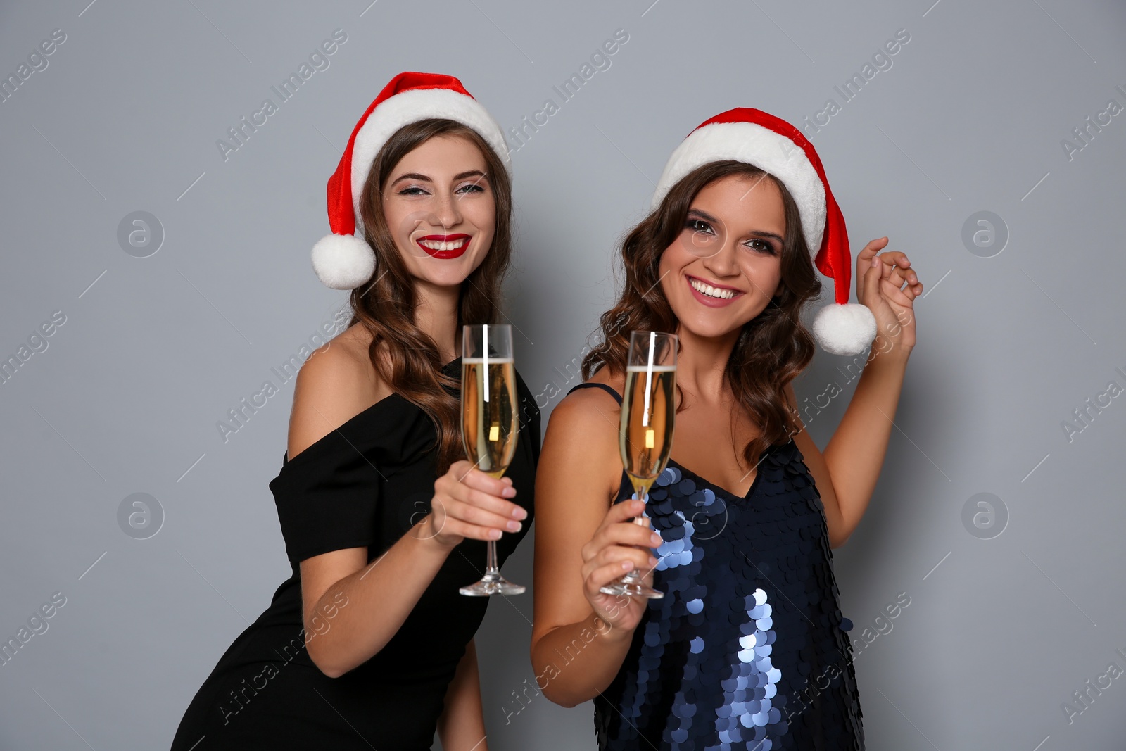 Photo of Happy women in Santa hats with champagne on grey background. Christmas party
