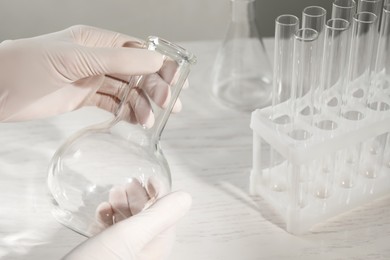 Photo of Scientist holding empty flask at white table, closeup