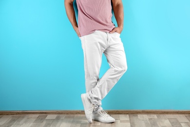 Photo of Young man in stylish jeans near color wall, focus on legs