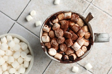Photo of Delicious hot chocolate with marshmallows, cocoa powder and spoon in cup on tiled table, top view