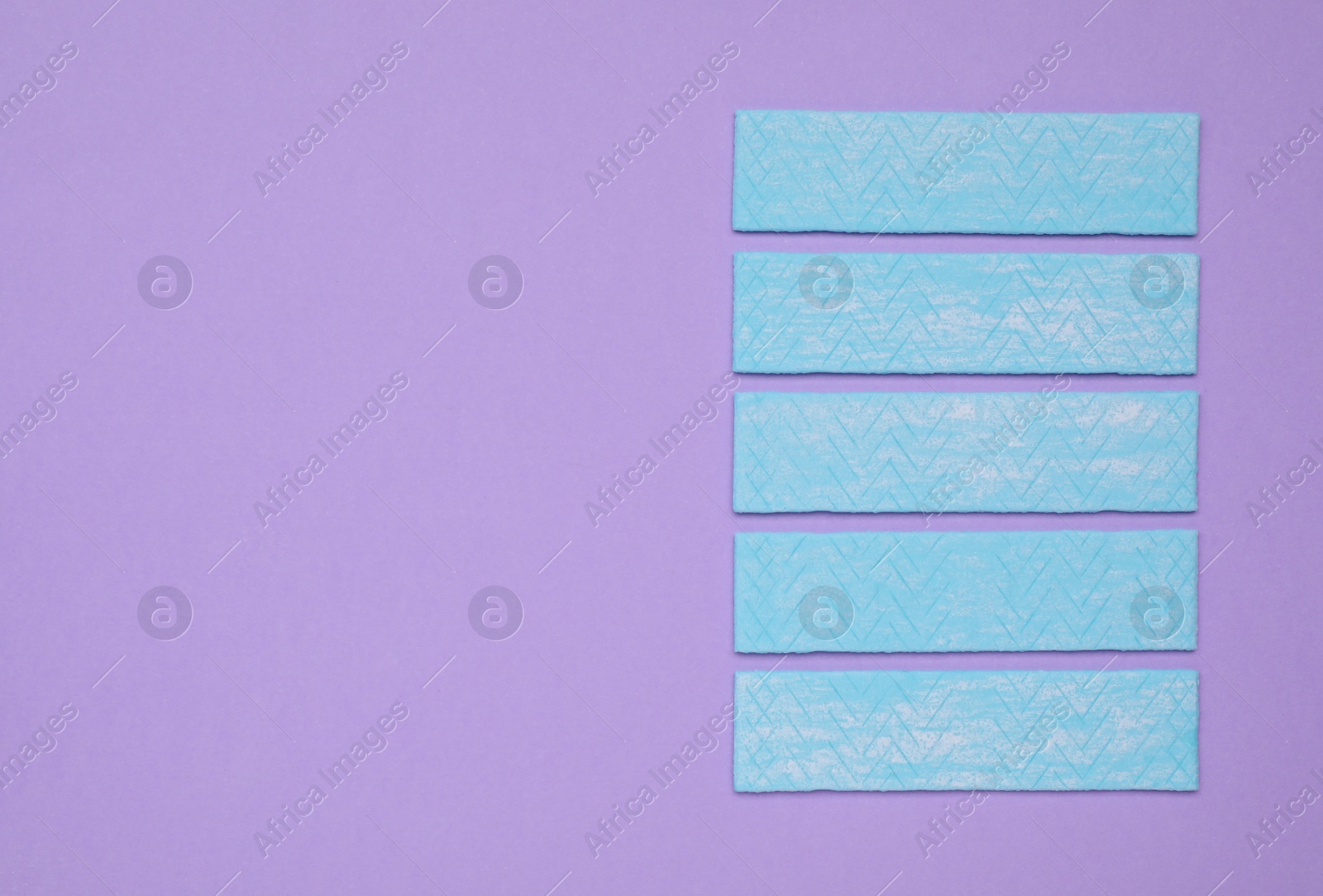 Photo of Many sticks of tasty chewing gum on violet background, flat lay. Space for text