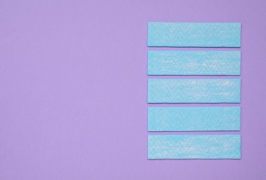 Photo of Many sticks of tasty chewing gum on violet background, flat lay. Space for text