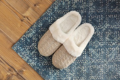 Pair of beautiful soft slippers and rug on wooden floor, top view