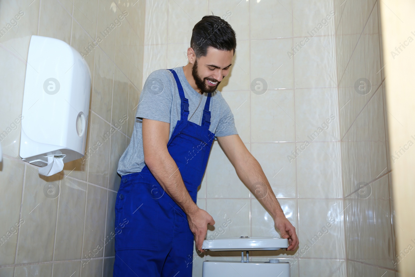 Photo of Male plumber repairing toilet tank in bathroom