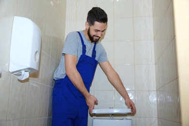 Male plumber repairing toilet tank in bathroom