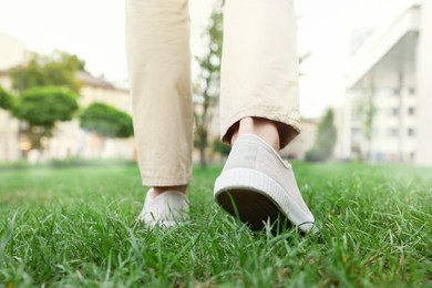 Photo of Man in stylish sneakers walking on green grass outdoors, closeup